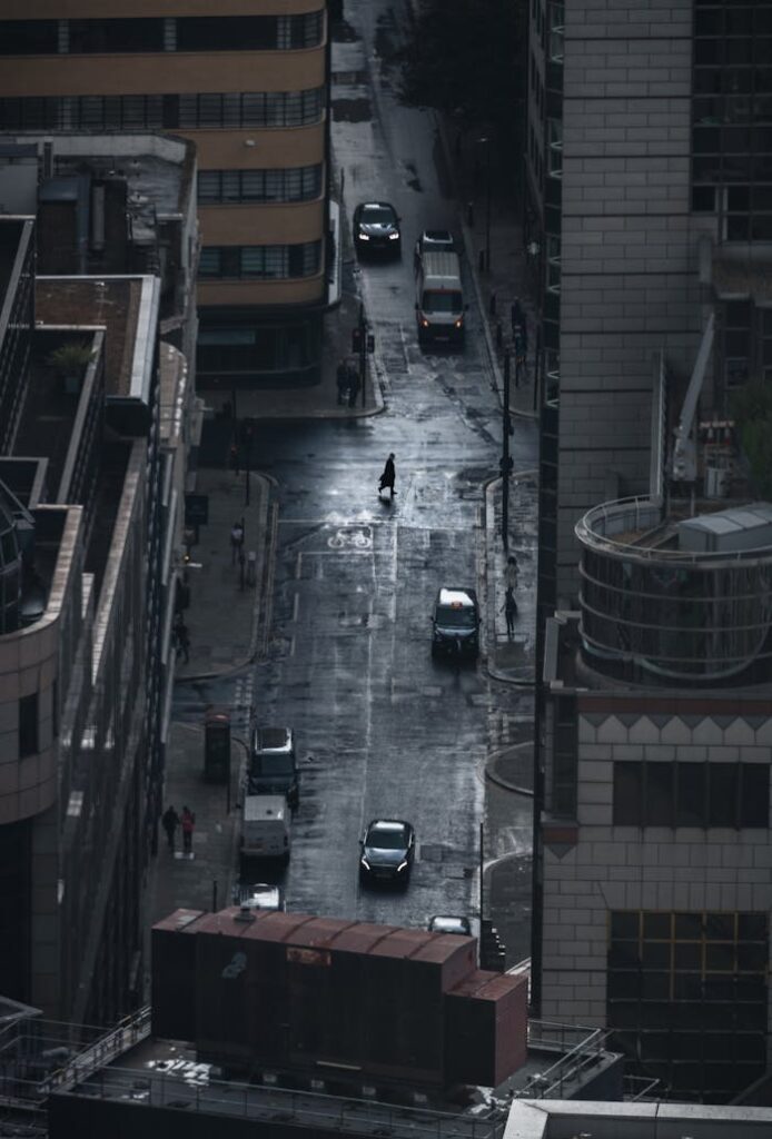 A dark, rainy street view of London with cars and a lone pedestrian under cloudy skies.